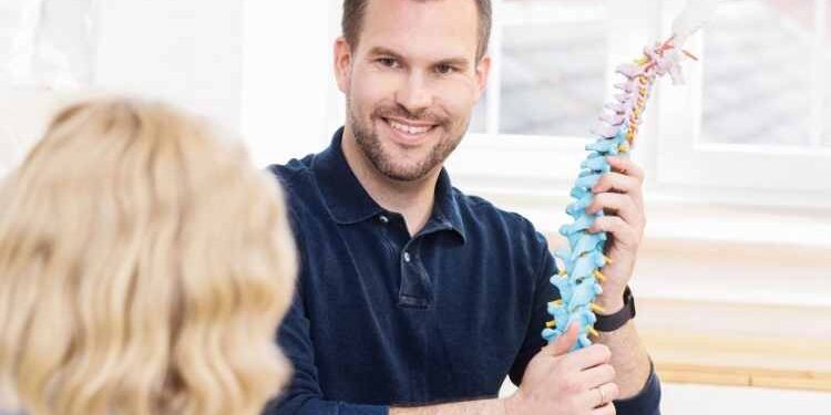 Arzt mit Blick zur Patientin, der eine Modell der Wirbelsäule in der Hand hat