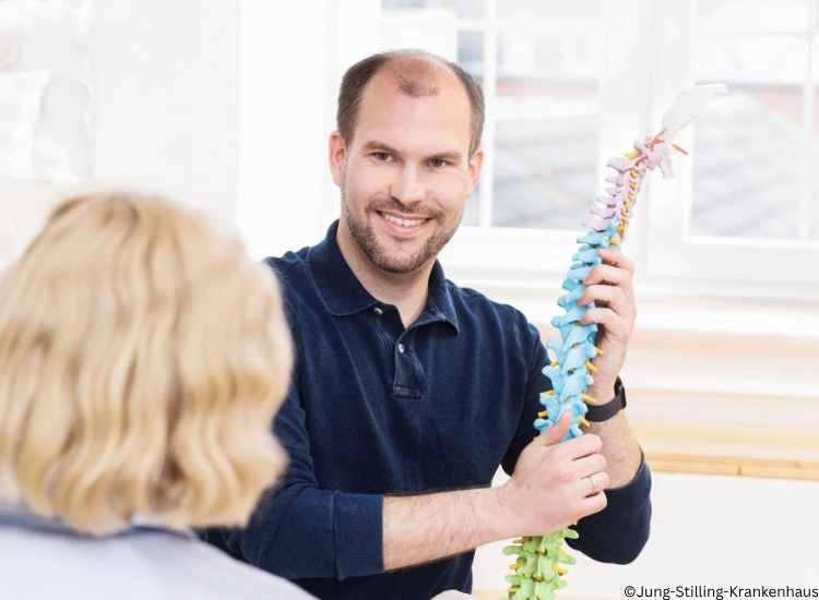 Arzt mit Blick zur Patientin, der eine Modell der Wirbelsäule in der Hand hat